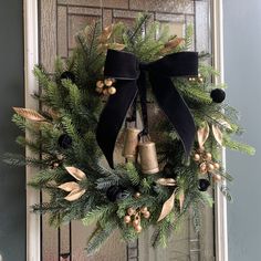 a wreath with bells and pine cones hanging from the front door, decorated with black ribbon