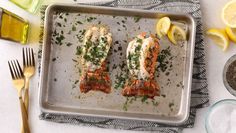 two salmon fillets on a baking sheet with lemons and spices next to them