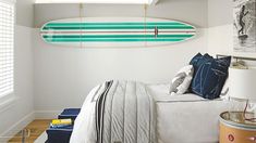 a surfboard hanging from the ceiling above a bed in a room with white walls