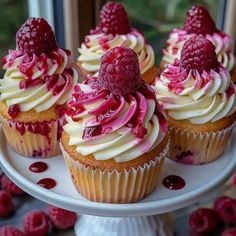 cupcakes with white frosting and raspberry toppings on a cake plate