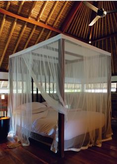 a canopy bed in a room with wooden floors and ceiling fans on either side of the bed