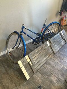 a blue bike parked next to a wooden bench on the floor in front of a wall