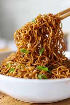 a bowl filled with noodles and chopsticks sitting on top of a wooden table