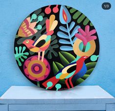 a colorful plate sitting on top of a white table next to a blue wall with plants and birds painted on it