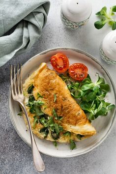 an omelet with spinach and tomatoes on a white plate next to silverware