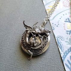 Gargoyle Dragon Guardian Protection Locket ☻Locket ~ Round Silver ~ With Bronze Bunny ~ With Flower ~ See Photos for size comparison against American quarter Chain: ~ Silver Plated YOU CHOOSE YOUR CHAIN LENGTH during checkout ☻More Lockets Here: https://www.etsy.com/shop/FashionCrashJewelry/search?search_query=lockets&order=date_desc&view_type=gallery&ref=shop_search ☻Link to The ENTIRE SHOP: https://www.etsy.com/shop/FashionCrashJewelry?ref=shopsection_shophome_leftnav&ga_search Antique Dragon Design Jewelry Gift, Antique Dragon Design Jewelry For Gift, Oxidized Silver Fantasy Jewelry, Fantasy Style Oxidized Jewelry Gift, Fantasy Style Oxidized Jewelry As A Gift, Fantasy Oxidized Finish Jewelry As A Gift, Silver Oxidized Fantasy Jewelry, Vintage Dragon Design Jewelry For Gifts, Vintage Dragon Design Jewelry Gift