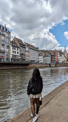 a woman walking along the side of a river next to tall buildings on both sides