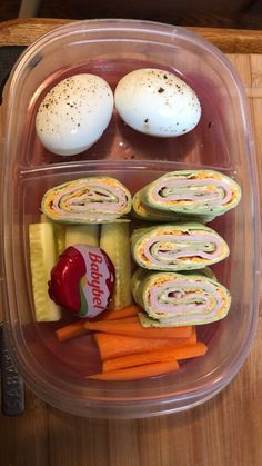 a plastic container filled with food on top of a wooden table next to an egg