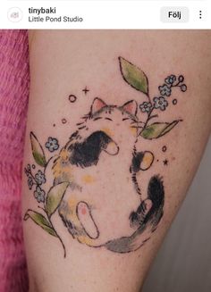 a cat tattoo on the leg of a woman's arm, with flowers and leaves around it