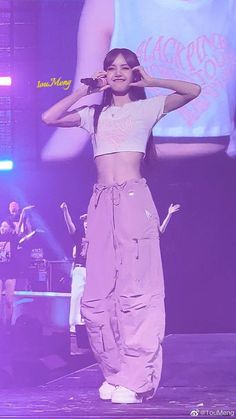 a woman standing on top of a stage with her hands behind her head while holding a microphone