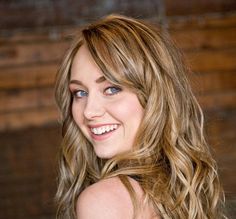 a close up of a person with long hair and blue eyes smiling at the camera