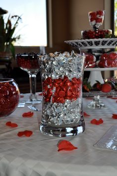 a table topped with lots of red candies next to wine glasses and plates filled with candy