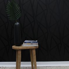 a wooden stool with a plant on top of it in front of a black wall