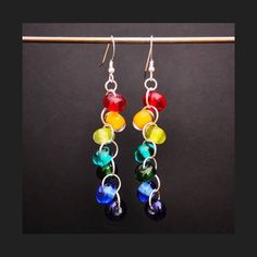 multicolored glass beaded earrings hanging from a hook on a wooden stick against a black background