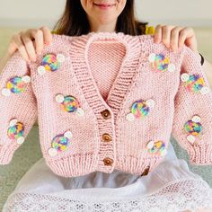 a woman holding up a pink cardigan with flowers on the front and back,