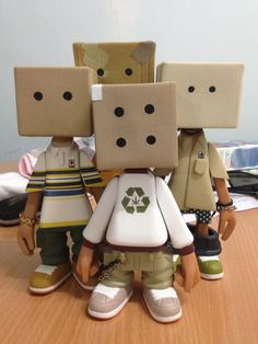 three small figurines made to look like people with boxes on their heads, sitting on a table