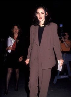 a woman in a brown suit and black top walking down the street with other people behind her