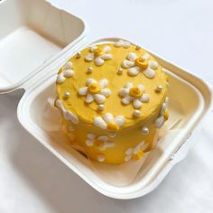 a yellow cake with white flowers on it in a plastic container next to an empty tray