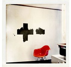 a red chair sitting in front of a wall with crosses on it's side