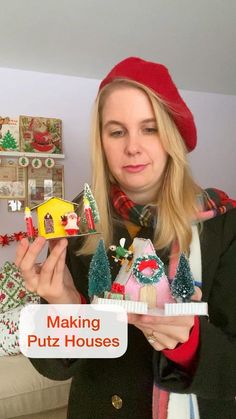 a woman in a red hat is holding up some christmas decorations and a doll house