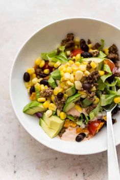 a white bowl filled with corn, black beans and avocado on top of a table