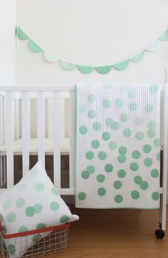 a white crib with a green polka dot blanket and two pillows on the floor