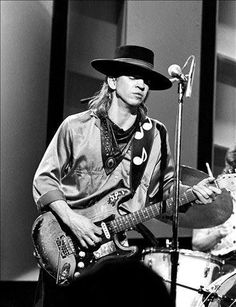 a man in a cowboy hat playing guitar and singing into a microphone while another man plays drums behind him