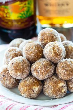 a white plate topped with sugar covered doughnuts next to a bottle of booze