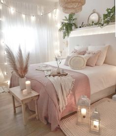 a white bed with pink sheets and pillows in a bedroom next to a window filled with lights