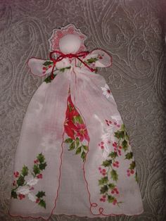 a white dress with holly leaves and red berries on it, sitting on a quilted surface