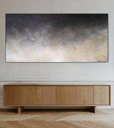 an abstract painting hangs on the wall above a wooden cabinet in a white living room