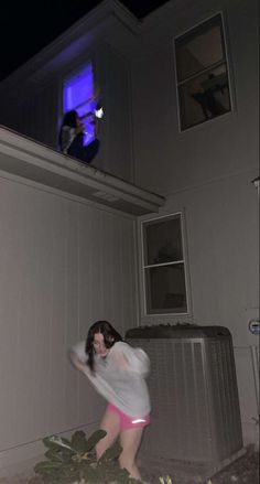 a woman in white shirt and pink shorts standing next to an air conditioner with blue light