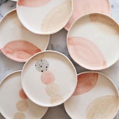 six plates with different designs on them sitting on a marble counter top, one is pink and the other is white