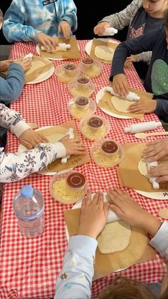 a group of children sitting at a table making pies with dough on paper plates