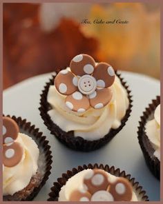 four cupcakes with white frosting and brown flowers on top are sitting on a plate