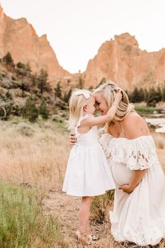 a mother and daughter hugging each other while standing in the grass with mountains in the background