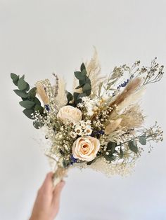 a hand holding a bouquet of flowers and greenery in front of a white wall