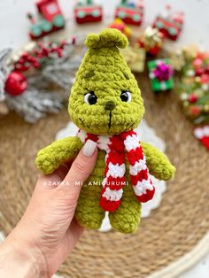 a hand holding a small green teddy bear with a red and white scarf around it's neck