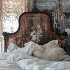 an old wooden bed with white linens in front of a rustic wall and window