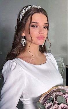 a woman wearing a white dress holding a bouquet of flowers in her hand and looking at the camera