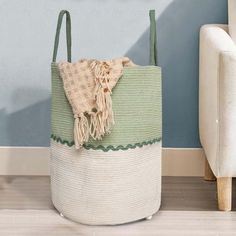 a green and white basket sitting on the floor next to a couch with a blue wall behind it