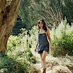 a woman walking down a dirt road next to a tree