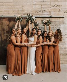 a group of women standing next to each other in front of a brick wall holding bouquets