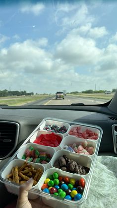 a person holding a tray filled with candy and candies in front of a car