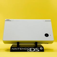 a nintendo ds game console sitting on top of a black and white stand against a yellow background