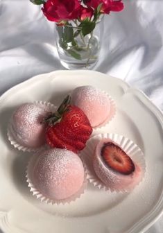 three desserts on a plate with strawberries and flowers in the vase behind them