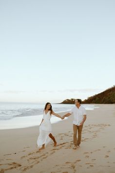 a man and woman holding hands while walking on the beach with footprints in the sand