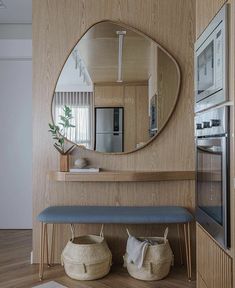 a mirror on the wall above a bench with two baskets under it and a potted plant next to it