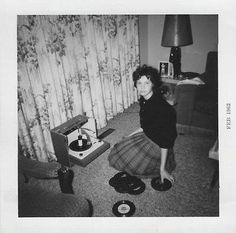 black and white photograph of a woman in a living room with record players on the floor