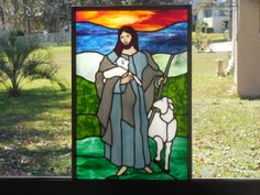 a stained glass window depicting jesus holding a lamb and standing in front of a house